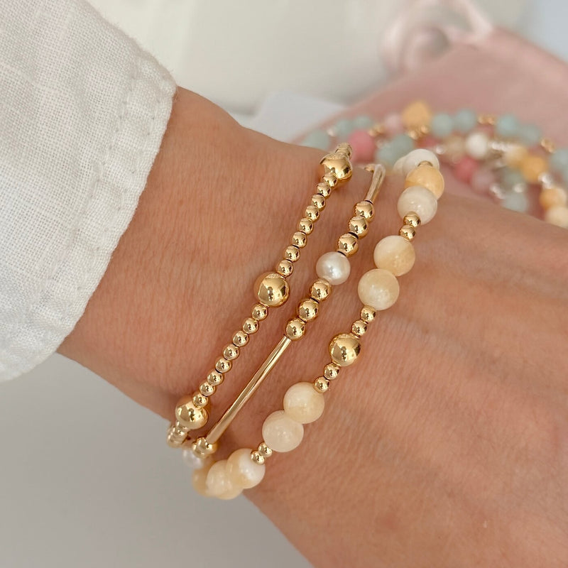 Close-up of a wrist wearing gold and pale lemon beaded bracelets on a neutral background