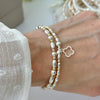 Silver and gold mixed metal, beaded bracelet duo with an open style studded four leaf clover on a wrist, with blurred jewellery in the background.
