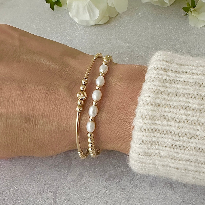 Two gold and pearl beaded bracelets on a wrist with a neutral background