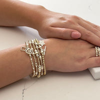 Close-up of a wrist wearing multiple silver and gold Bella Jane beaded stacking bracelets on a light background