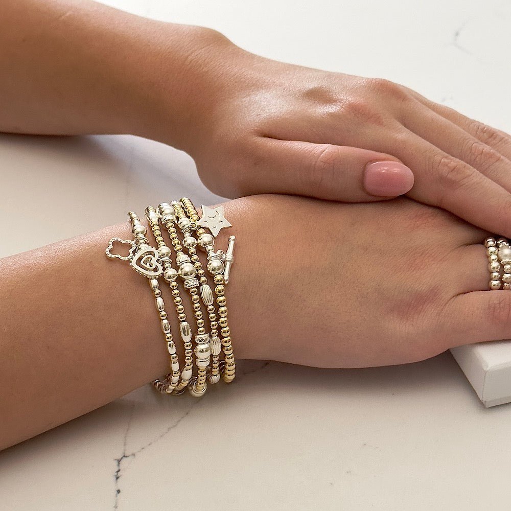 Close-up of a wrist wearing multiple silver and gold Bella Jane beaded stacking bracelets on a light background