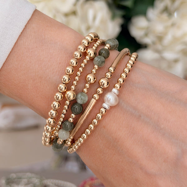 A lady's wrist with gold beaded stacking bracelets, one featuring olive green beads