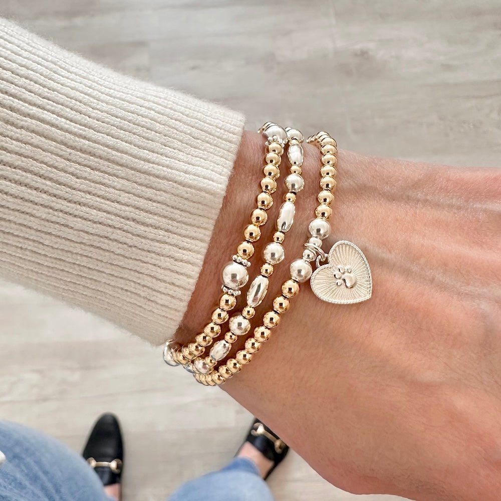 A stack of sterling silver and gold stacking bracelets featuring the Paw Prints on My Heart bracelet