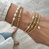 Close-up of a wrist wearing gold and pearl beaded stacking bracelets on a light background