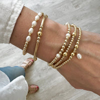 Close-up of a wrist wearing gold and pearl beaded stacking bracelets on a light background