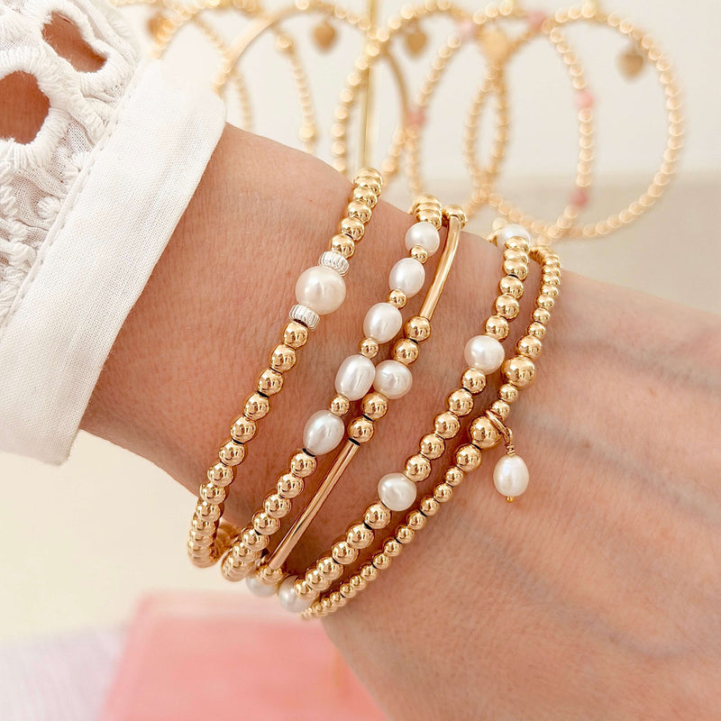 A close up of a lady's wrist wearing 5 Bella Jane gold  beaded bracelets with freshwater pearls
