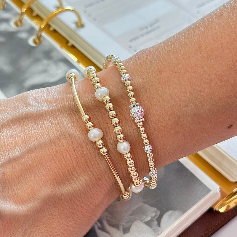 Gold and pearl beaded bracelets on a wrist with a blurred background