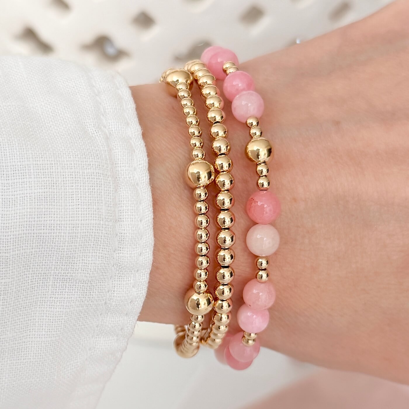 A lady's wrist wearing 3 gold-filled beaded stacking bracelets, one with pastel pink beads for summer
