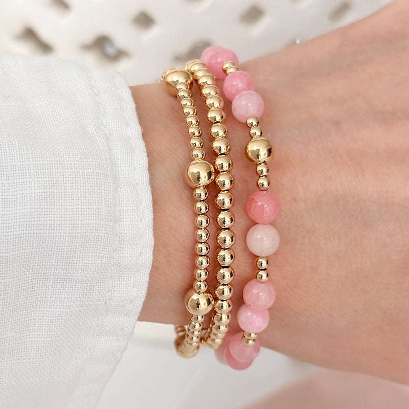 A lady's wrist wearing 3 gold-filled beaded stacking bracelets, one with pastel pink beads for summer