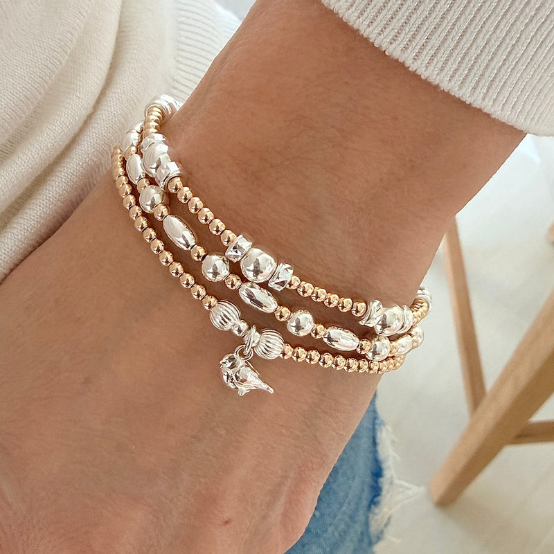 A close-up of a person's wrist wearing three sterling silver and gold-filled beaded bracelets. One bracelet featuring a shiny sterling silver robin charm.