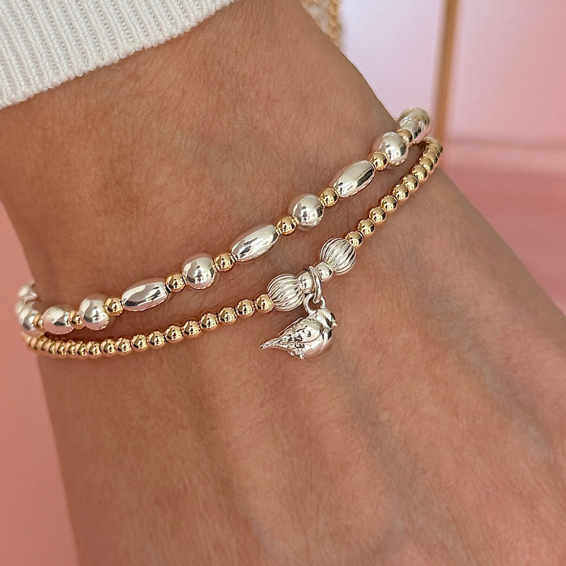 A close-up of a person's wrist wearing two sterling silver and gold-filled mixed metal beaded bracelets: one featuring a sterling silver robin charm