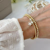 A ladies wrist wearing a silver and gold mixed metal beaded bracelet duo with a silver star charm, with a blurred background of flowers.