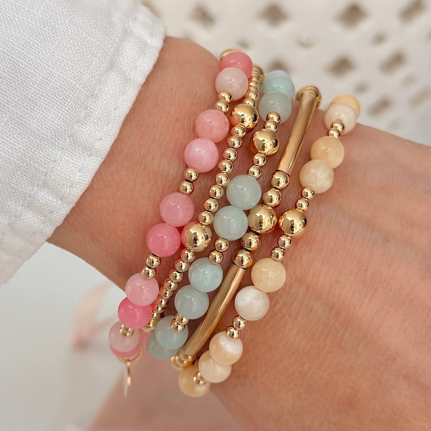 Stack of pastel and gold beaded bracelets on a hand with a blurred background