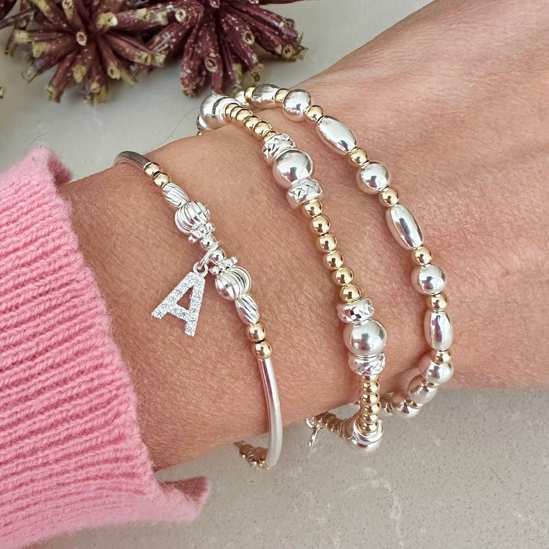Bracelets with beads and a letter 'A' charm on a wrist, wearing a pink sleeve.