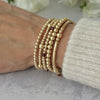 Gold beaded stacking bracelets on a wrist, one featuring tiny deep garnet coloured beads, against a neutral background