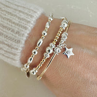 A close up of gold and silver mixed metal beaded stacking bracelets, one featuring a small star charm with a tiny cubic zirconia stone in centre of the charm, on a wrist against a neutral background