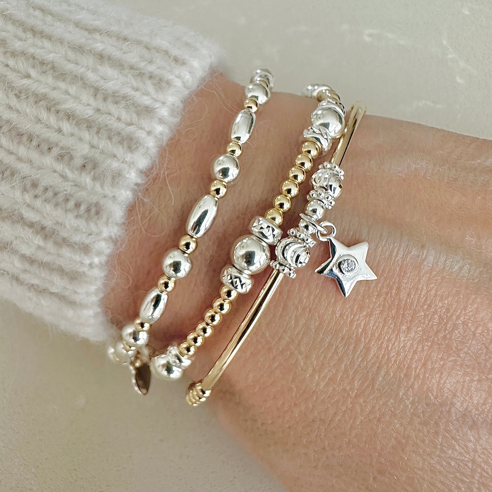 A close up of gold and silver mixed metal beaded stacking bracelets, one featuring a small star charm with a tiny cubic zirconia stone in centre of the charm, on a wrist against a neutral background