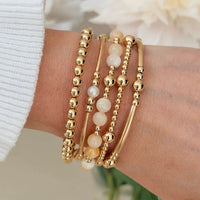Gold beaded bracelets with pale lemon jade and freshwater pearl beads, on a wrist with a blurred background