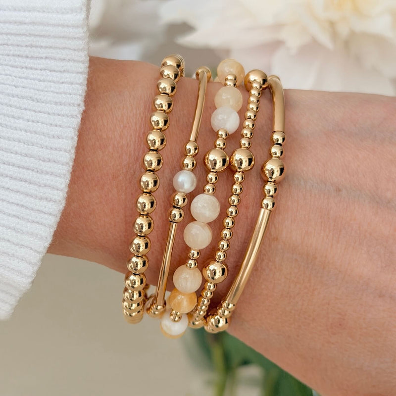 Gold beaded bracelets with pale lemon jade and freshwater pearl beads, on a wrist with a blurred background