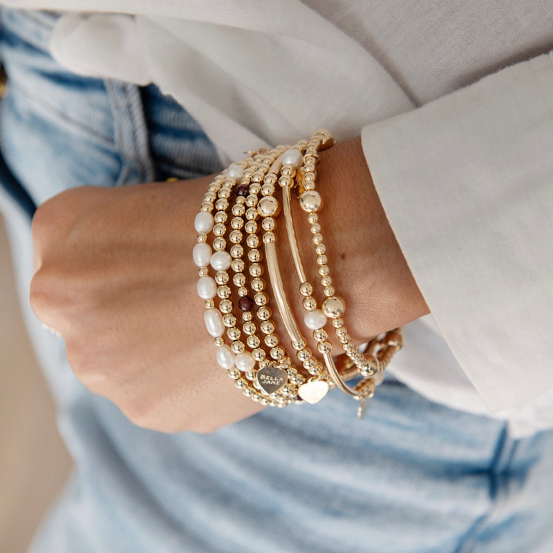 Close-up of a wrist wearing multiple gold and pearl bracelets with a blurred background.