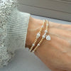 Two gold and silver mixed-metal beaded stacking bracelets, one with a heart charm on a wrist, against a neutral background