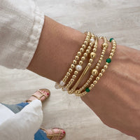 Gold beaded bracelets on a wrist, featuring green onyx beads with a blurred background