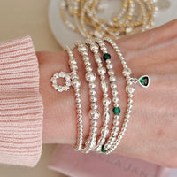 Close-up of a wrist wearing multiple silver beaded bracelets with green accents.