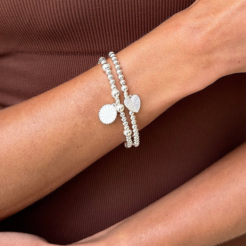 Silver bracelet with heart charms on a wrist against a brown background
