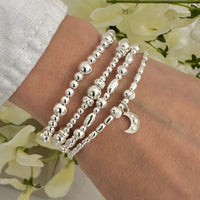 Silver beaded bracelets on a wrist with a floral background, one bracelet featuring a sterling silver and ivory enamel moon charm, with tiny stars