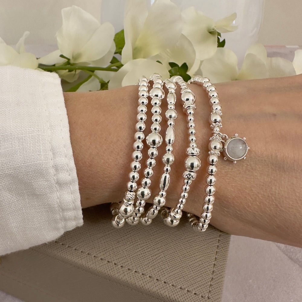 Silver beaded bracelets on a wrist , one featuring a silver and moonstone charm, with a neutral background