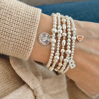 Close-up of a wrist wearing multiple sterling silver beaded stacking bracelets with charms.