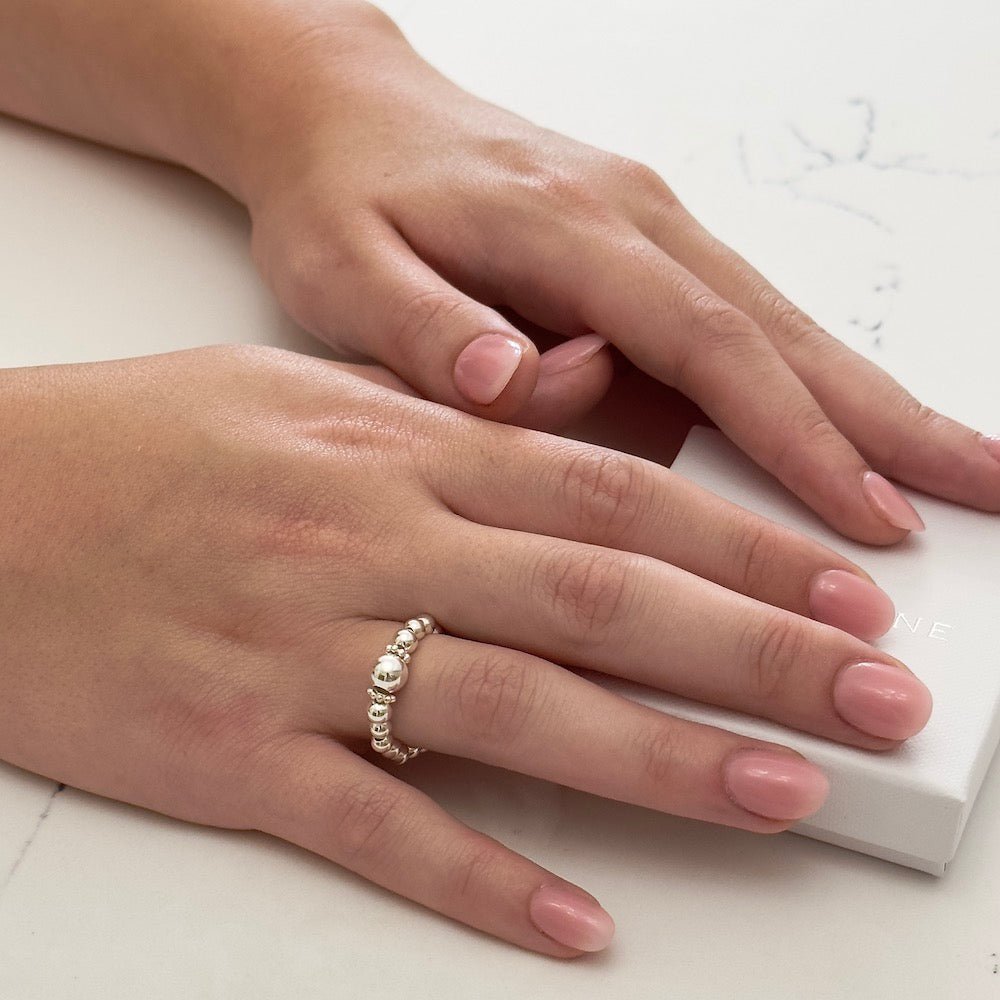 Close-up of a hand wearing a silver beaded stacking ring on a light background