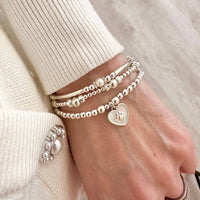 A stack of sterling silver stacking bracelets featuring the Paw Prints on My Heart bracelet
