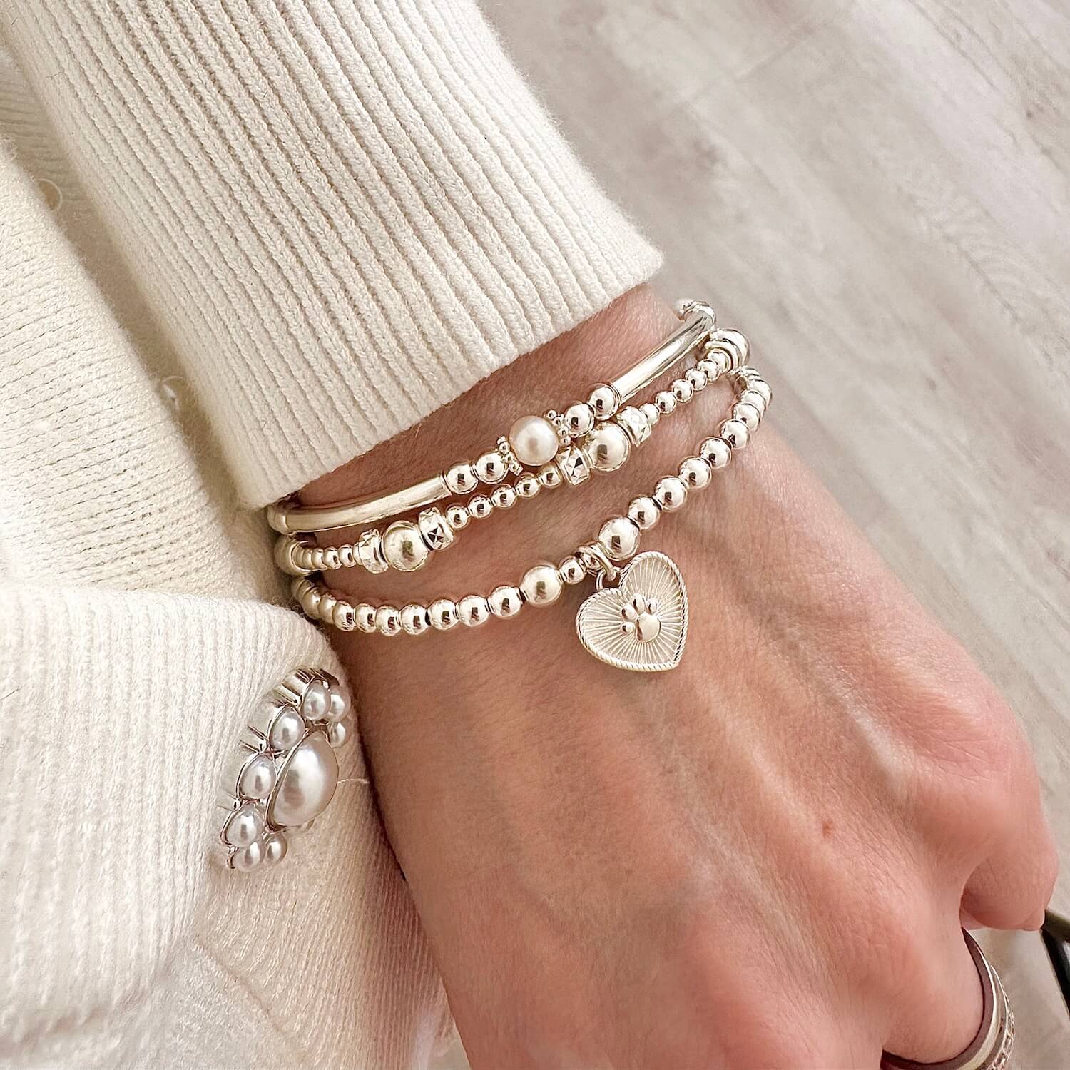 A stack of sterling silver stacking bracelets featuring the Paw Prints on My Heart bracelet