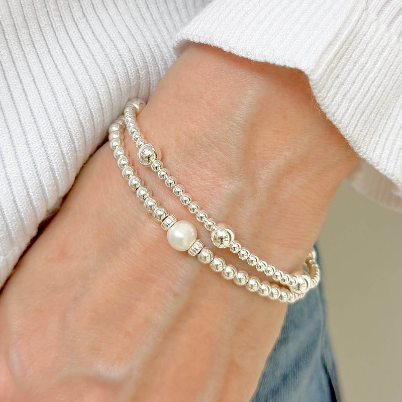 Close-up of a hand wearing a silver beaded bracelet duo, with one bracelet featuring a large focal pearl in the centre. 