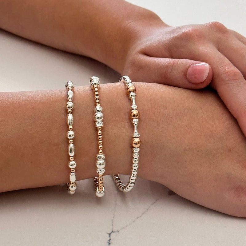 Close up of hands wearing gold and silver beaded bracelets on a light background