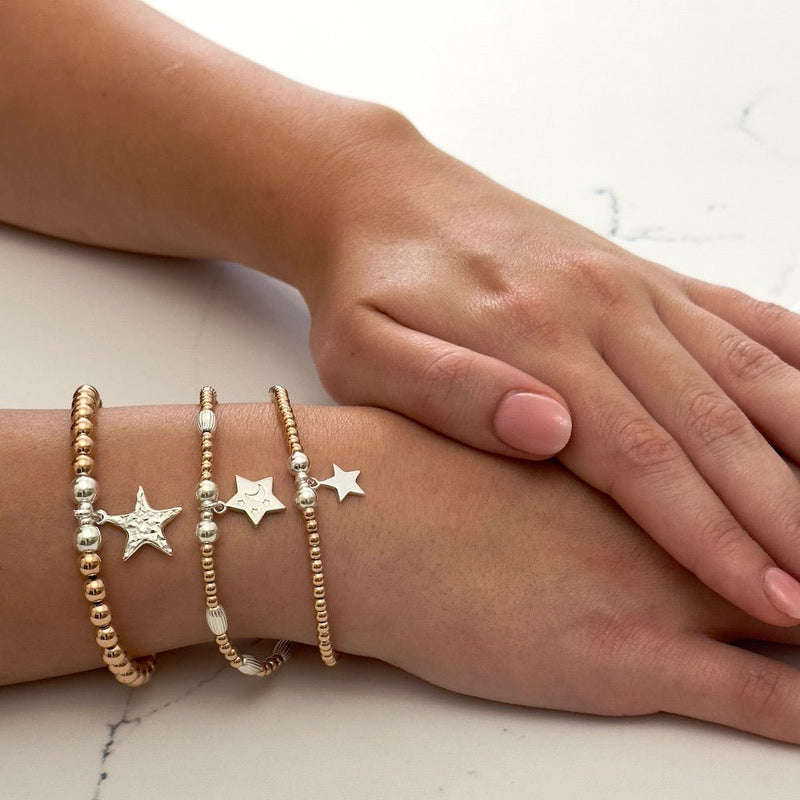 Close-up of a hand wearing multiple star charm stacking bracelets on a light background