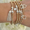 Stack of rose gold and silver beaded bracelets on a wrist with a blurred floral background
