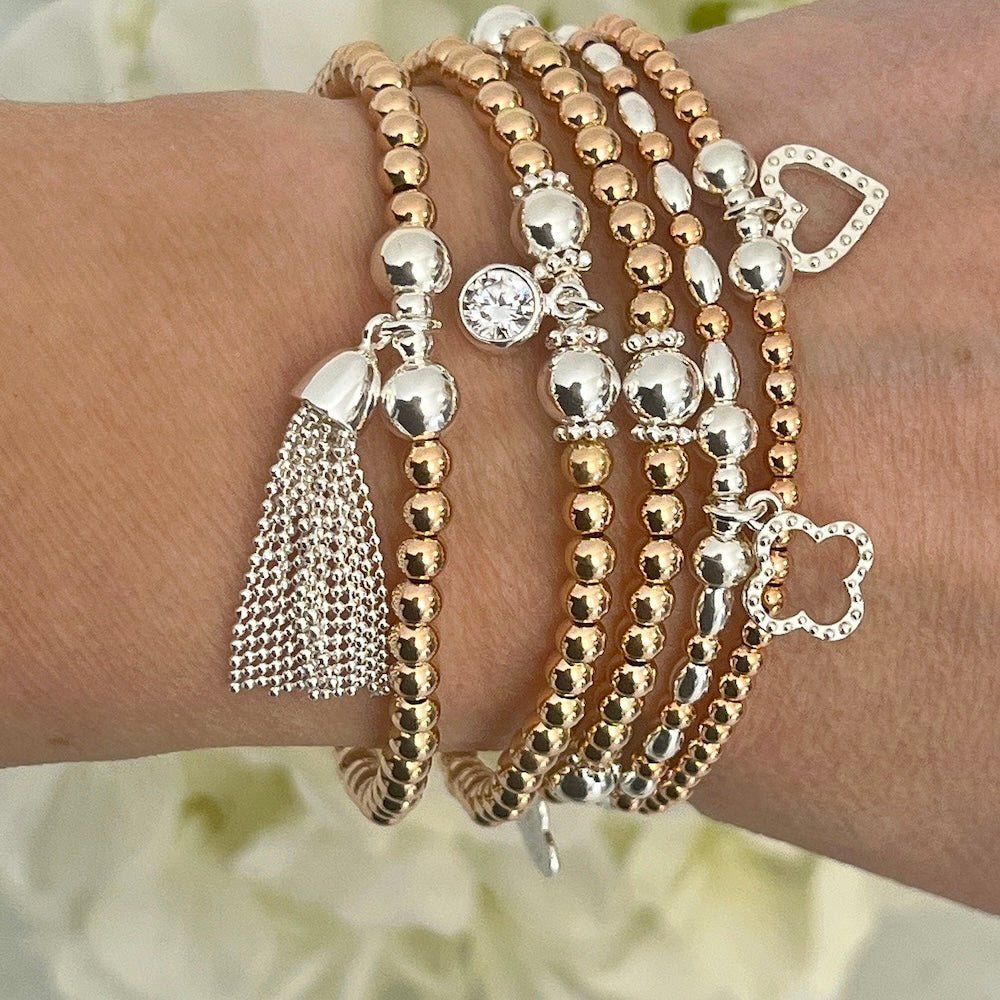 Stack of rose gold and silver beaded bracelets on a wrist with a blurred floral background