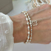 Silver and roe gold mixed metal, beaded bracelet duo with an open style studded four leaf clover on a wrist, with blurred jewellery in the background.