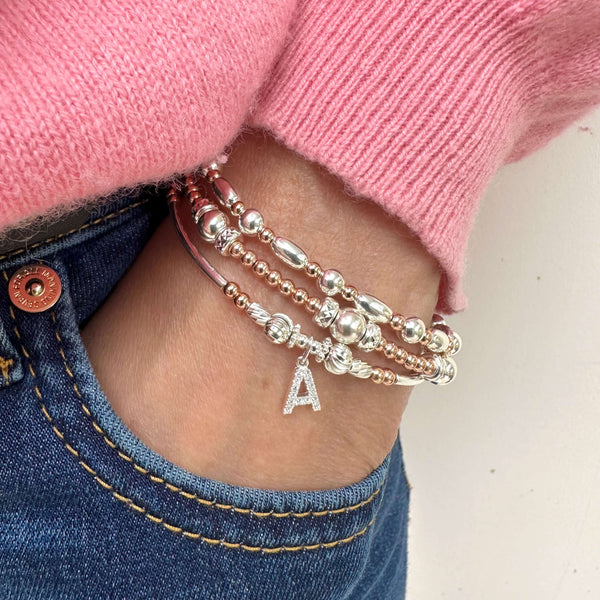 Close-up of a person's wrist wearing multiple bracelets with a pink sweater and blue jeans.