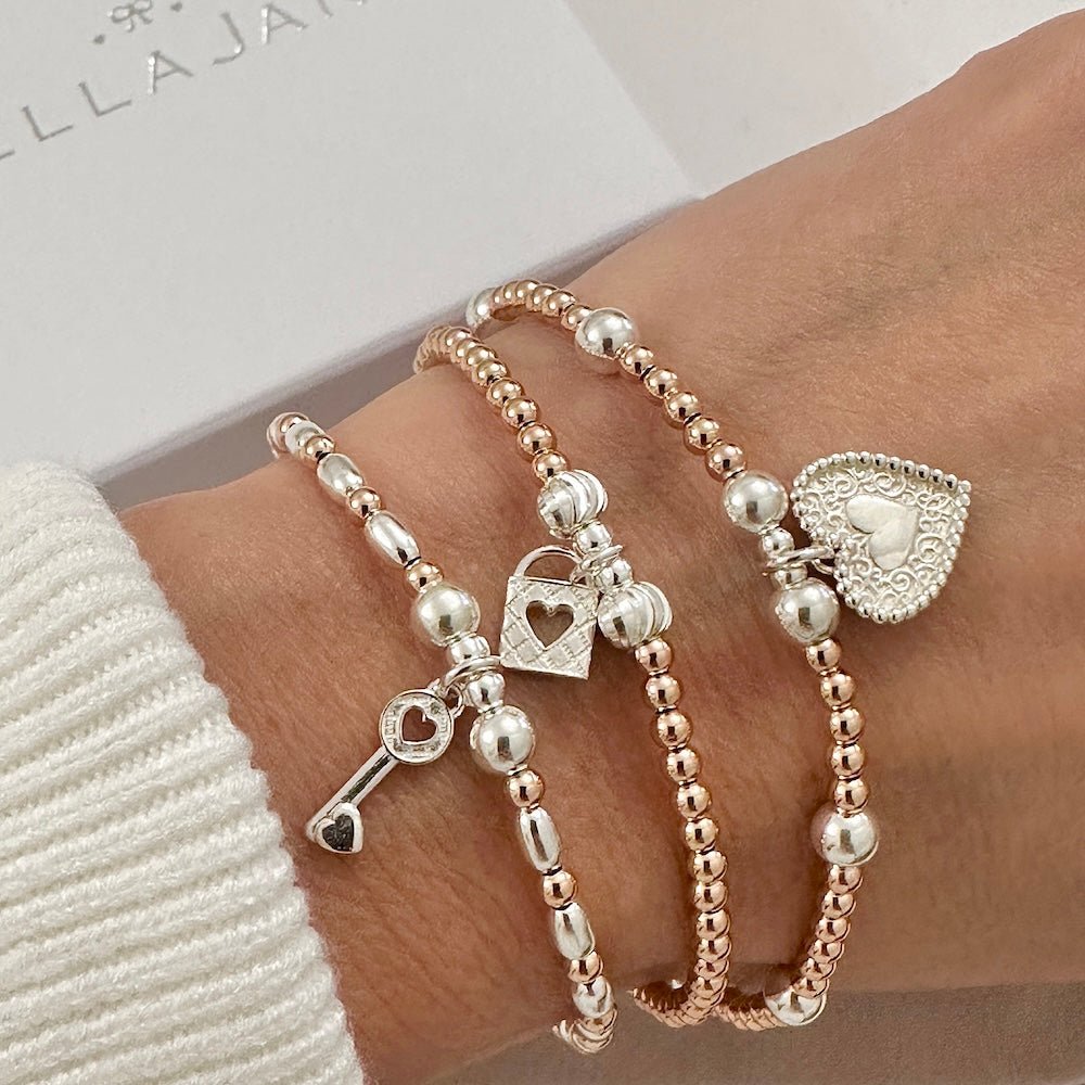 Three beaded rose gold and sterling silver bracelets with heart, padlock and key charms, on a wrist with a white sleeve