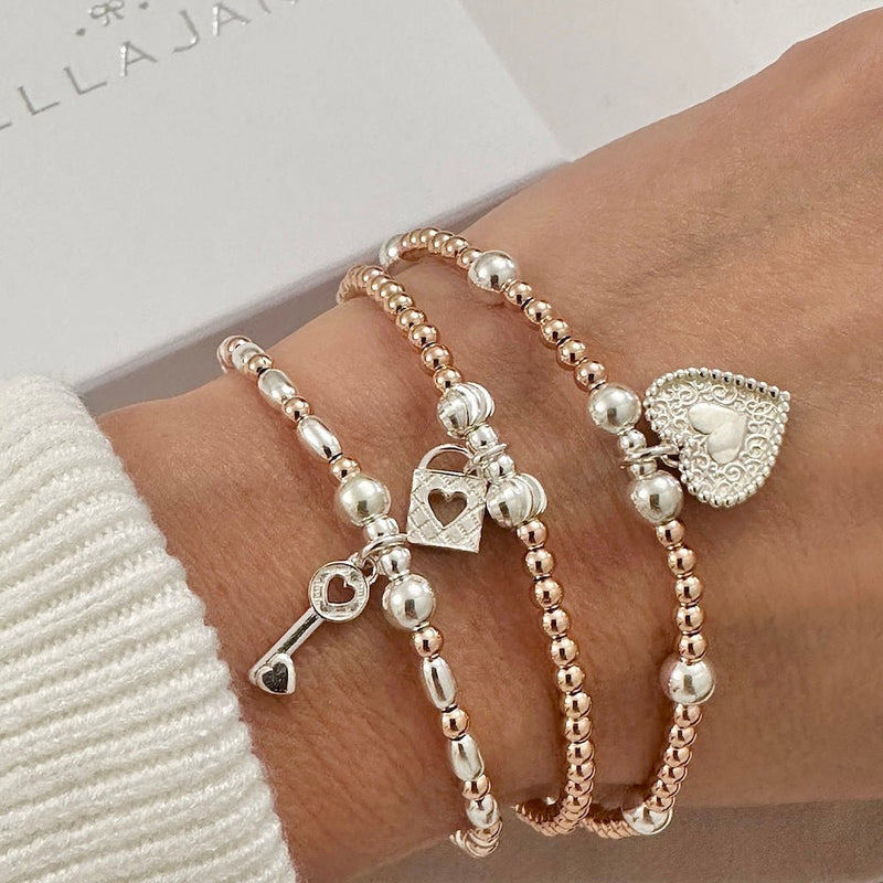 Three beaded rose gold and sterling silver bracelets with heart, padlock and key charms, on a wrist with a white sleeve