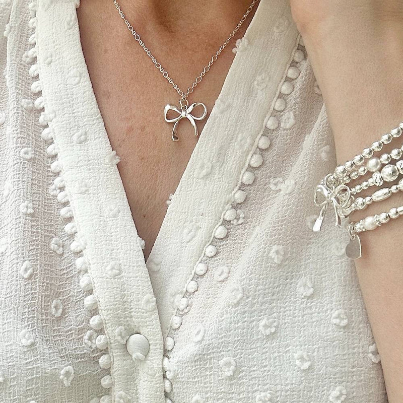 A lady wearing a delicate sterling silver chain with silver bow pendant.