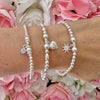 Silver beaded bracelets with sparkly charms on a wrist against a floral background