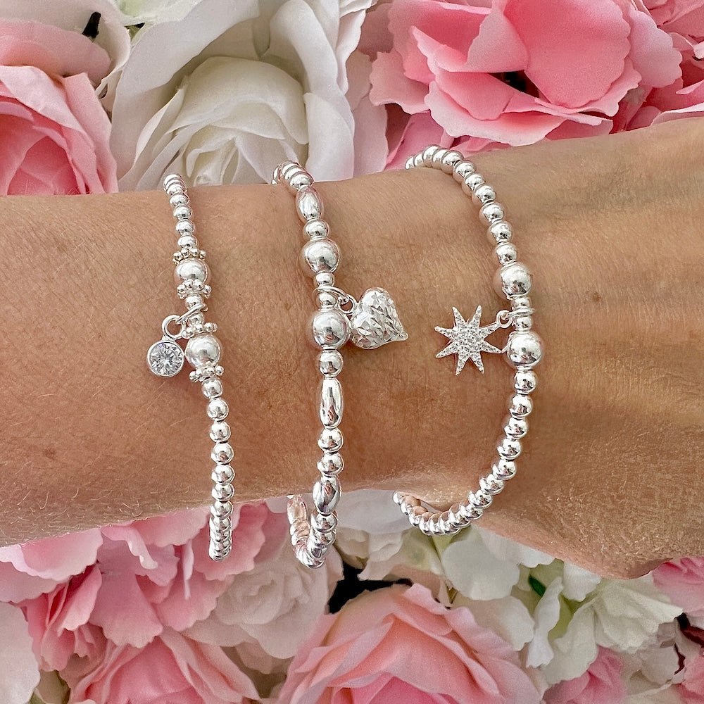 Silver beaded bracelets with sparkly charms on a wrist against a floral background