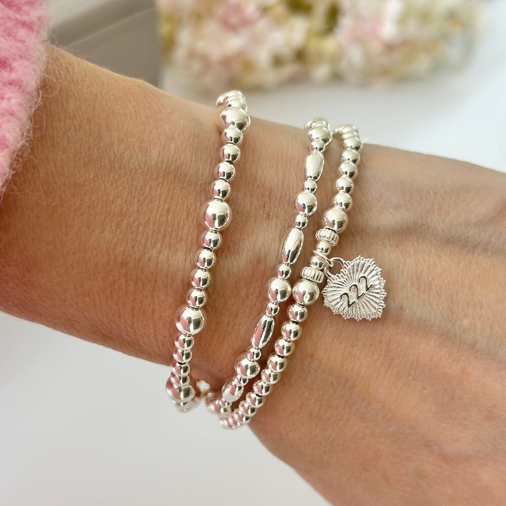 A close up photo of a woman's wrist, featuring 3 sterling silver beaded stacking bracelets, one with a heart-shaped charm featuring angel number 222 on the front of the charm.