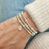 Silver beaded bracelet with a teardrop charm, with two other silver beaded stacking bracelets, on a wrist against a denim background
