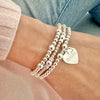 Three silver beaded bracelets with a heart-shaped charm on one of the bracelets, engraved with the word 'Bestie' -  on a wrist against a denim jeans background.