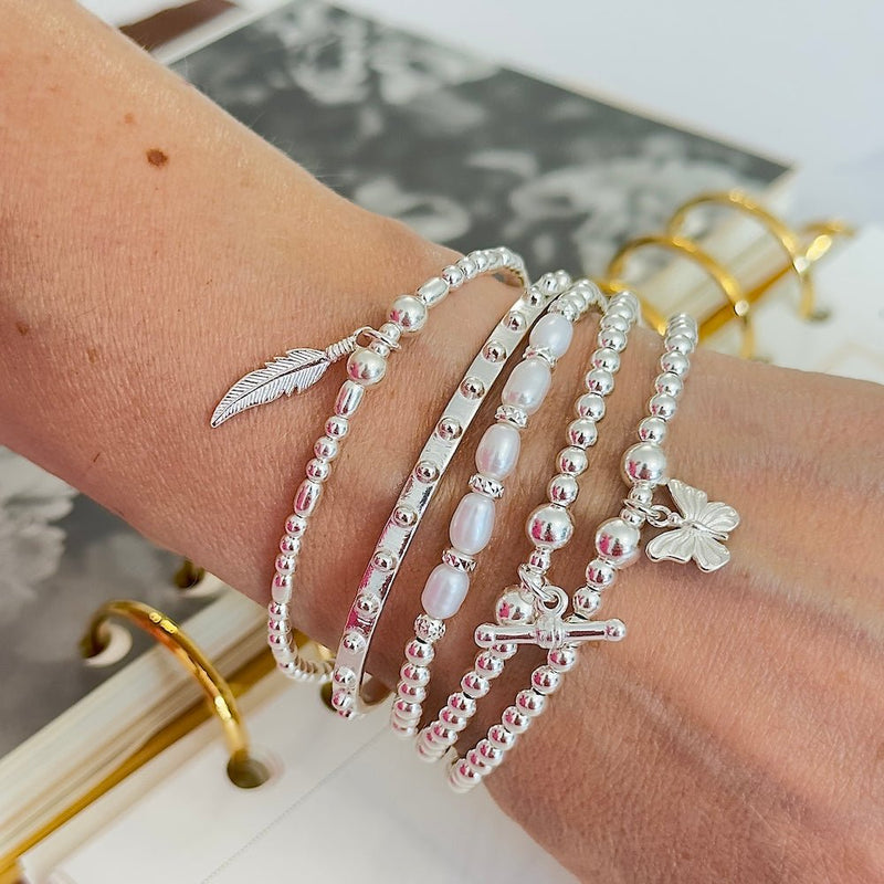 Close-up of a wrist wearing multiple silver and pearl bracelets with charms on a blurred background.